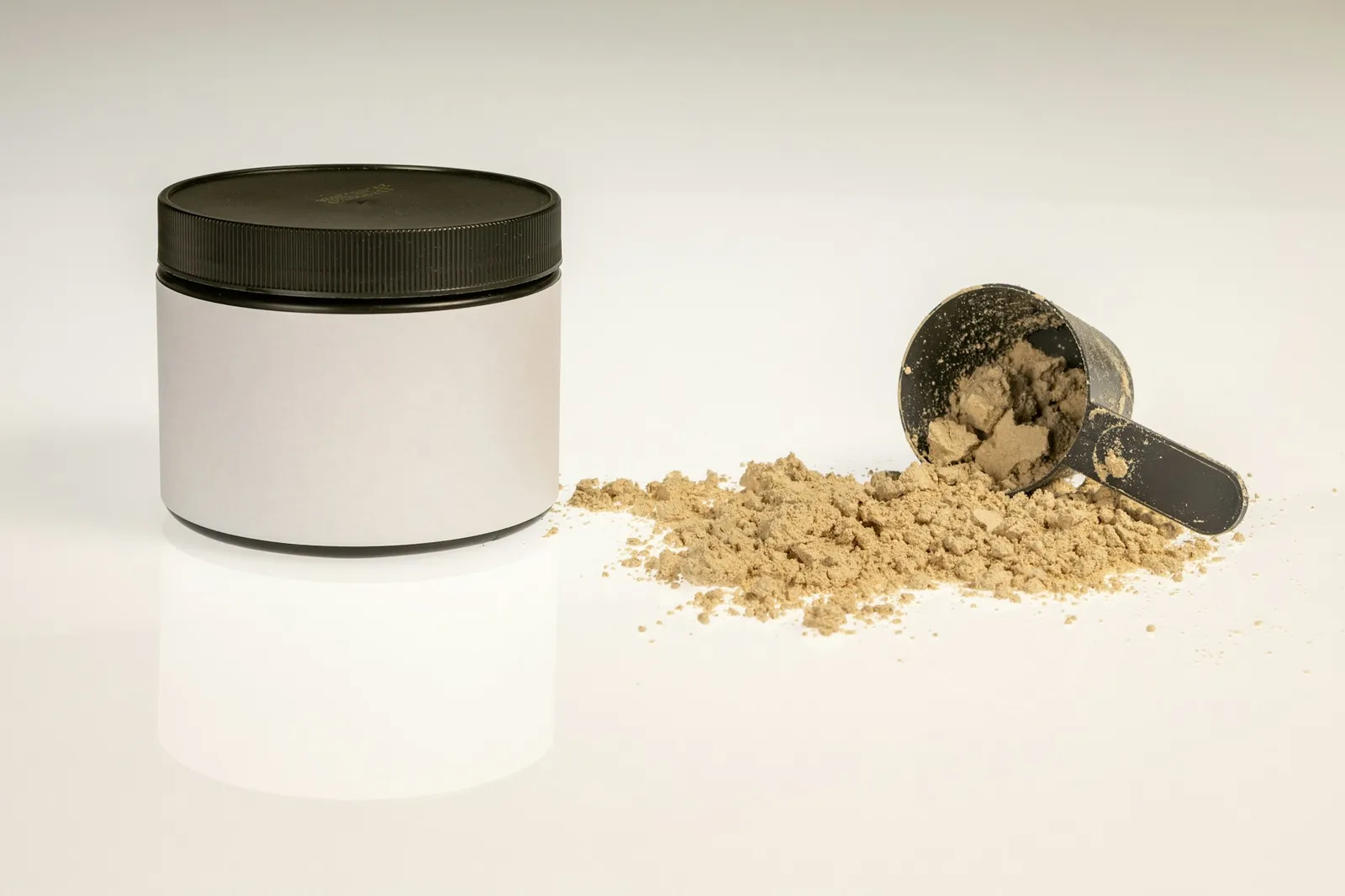 A supplement tub beside a scoop and a spill of powder