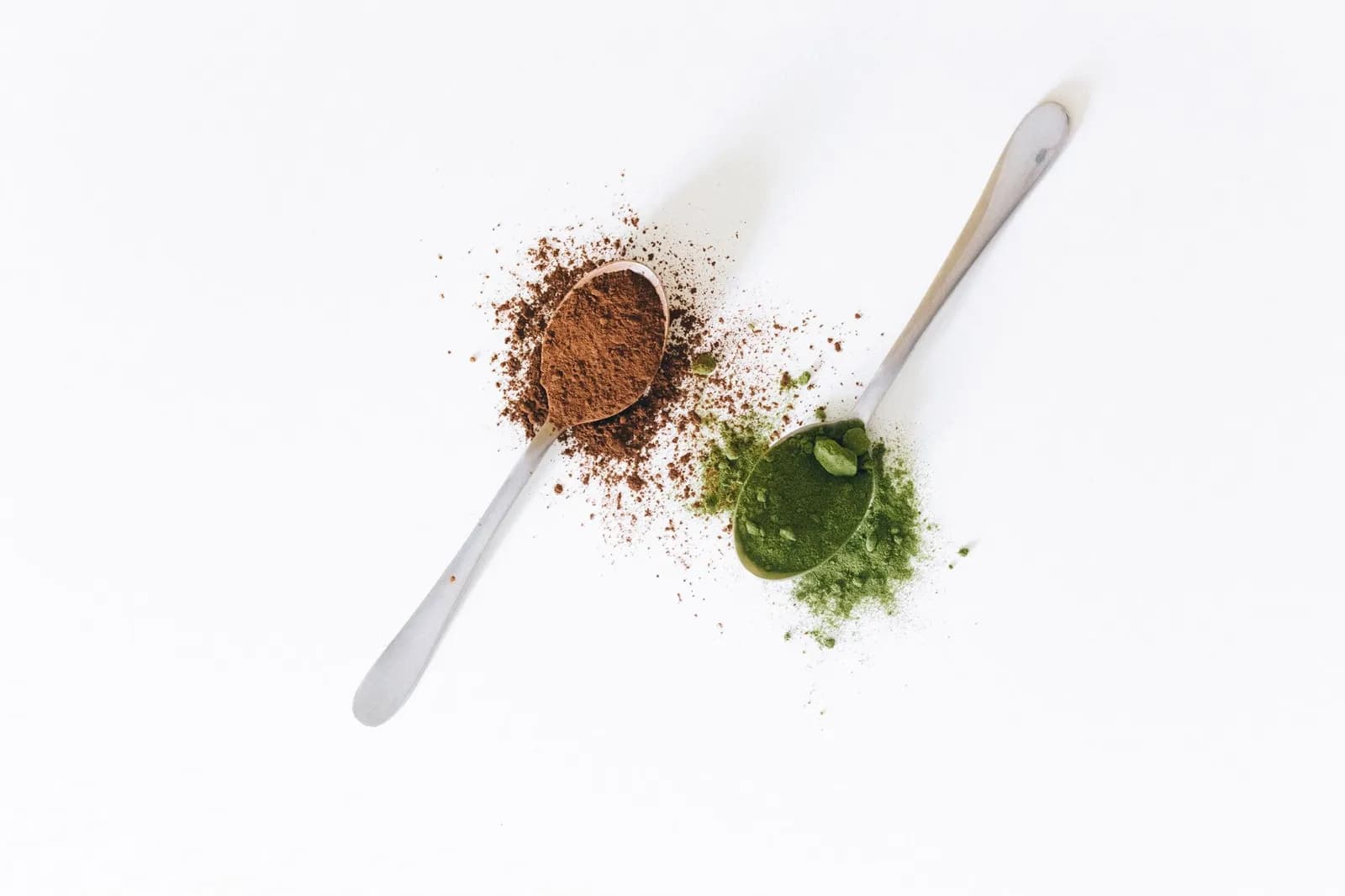 Two spoons of contrasting powders side by side on a white surface